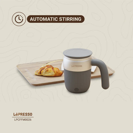 Le'Presso automatic stirring mug with a croissant on a wooden board, on a beige background.