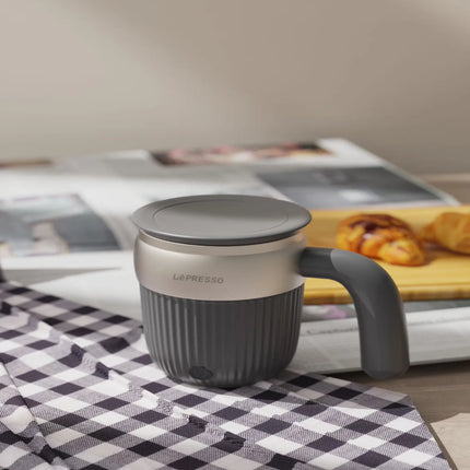 Gray coffee mug with handle on a checkered tablecloth, newspaper, and pastry in the background