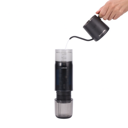 Hand pouring liquid into a black and gray coffee maker on a white background
