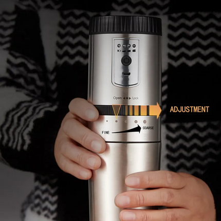 Hand holding a silver coffee grinder with adjustment settings on a dark background