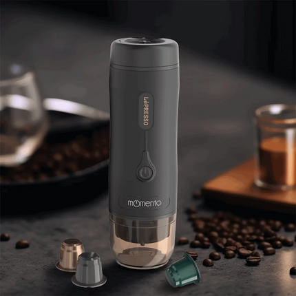 Gray coffee pod device with 'Le'PRESSO' branding on a dark surface with coffee beans and a glass of water.