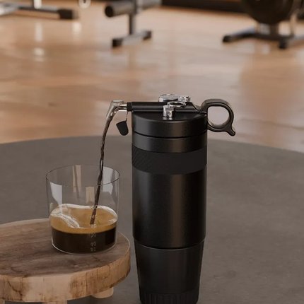 Black travel mug with a wooden coaster and glass of coffee in a gym setting
