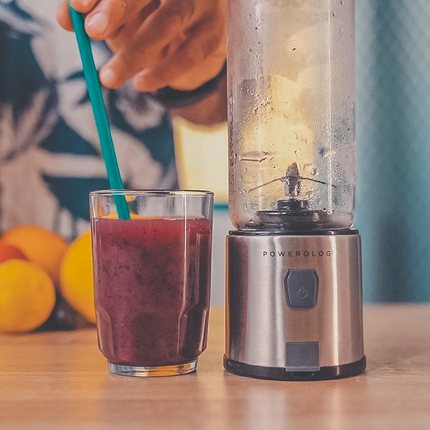 Beverage mixer with a glass of juice and straw on a wooden surface